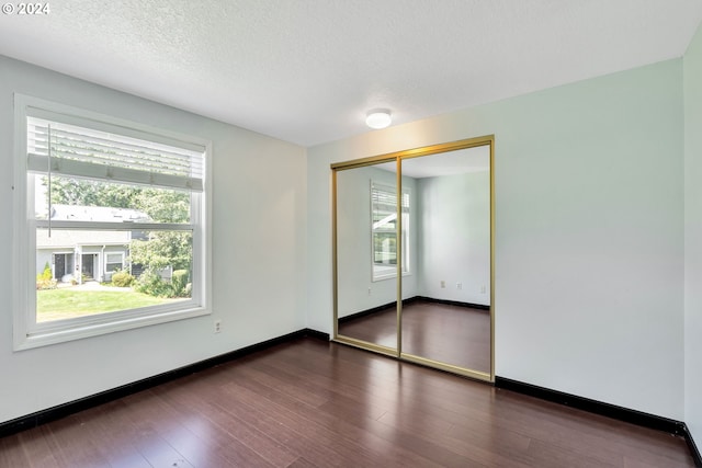 unfurnished bedroom featuring a closet, dark hardwood / wood-style floors, a textured ceiling, and multiple windows