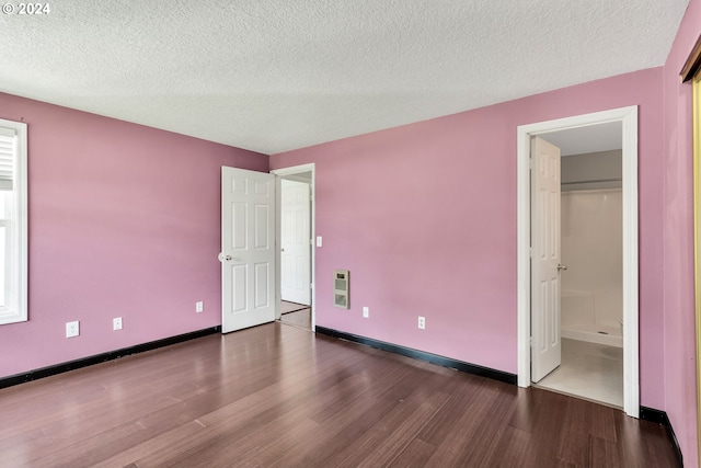 unfurnished bedroom featuring heating unit, connected bathroom, dark hardwood / wood-style floors, and a textured ceiling