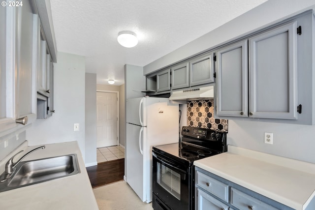 kitchen featuring a textured ceiling, black / electric stove, white refrigerator, tasteful backsplash, and sink