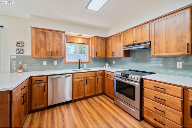 3427 NE 32nd Pl, Portland, OR 97212 - kitchen featuring appliances with stainless steel finishes, under cabinet range hood, a sink, light wood-type flooring, and brown cabinetry
