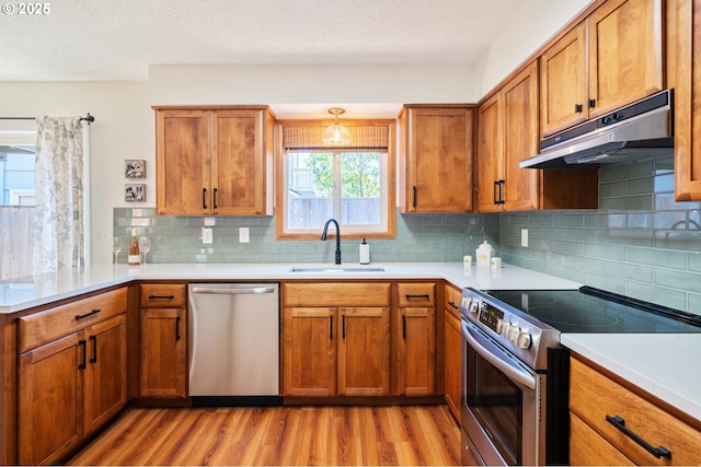 3427 NE 32nd Pl, Portland, OR 97212 - kitchen with appliances with stainless steel finishes, under cabinet range hood, a sink, light wood finished floors, and a peninsula