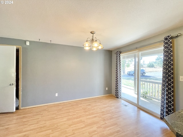 empty room with light hardwood / wood-style floors, a textured ceiling, and an inviting chandelier