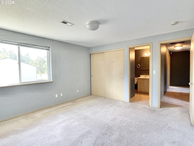 unfurnished bedroom featuring connected bathroom, light carpet, a closet, and a textured ceiling