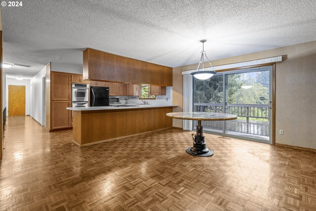 kitchen with brown cabinetry, freestanding refrigerator, visible vents, a peninsula, and light countertops