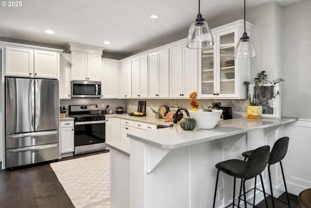 kitchen featuring appliances with stainless steel finishes, white cabinetry, glass insert cabinets, and a peninsula