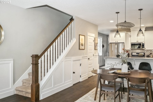 dining space with dark wood-style floors, stairway, a decorative wall, and a wainscoted wall