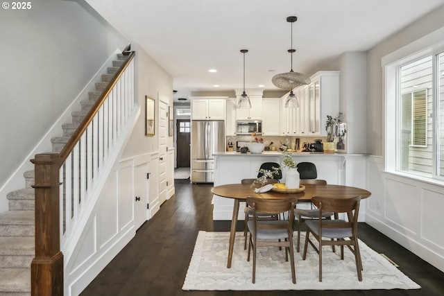 dining area featuring dark wood-style floors, recessed lighting, wainscoting, a decorative wall, and stairs