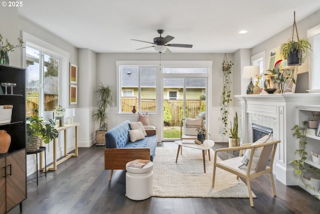 living area with ceiling fan, a wainscoted wall, wood finished floors, and a tiled fireplace