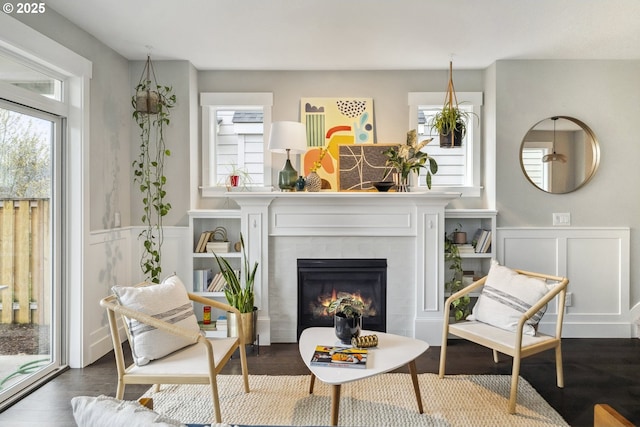 sitting room with dark wood-style flooring, a glass covered fireplace, wainscoting, and a decorative wall