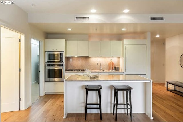 kitchen with light wood-style floors, visible vents, a kitchen breakfast bar, and built in appliances