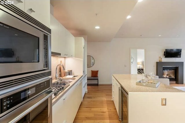 kitchen featuring light wood-style flooring, stainless steel appliances, a sink, white cabinets, and a center island