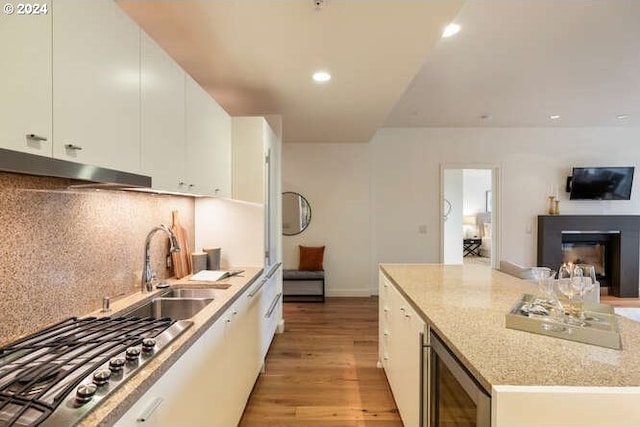 kitchen featuring wine cooler, white cabinetry, light wood-style floors, a center island, and a glass covered fireplace