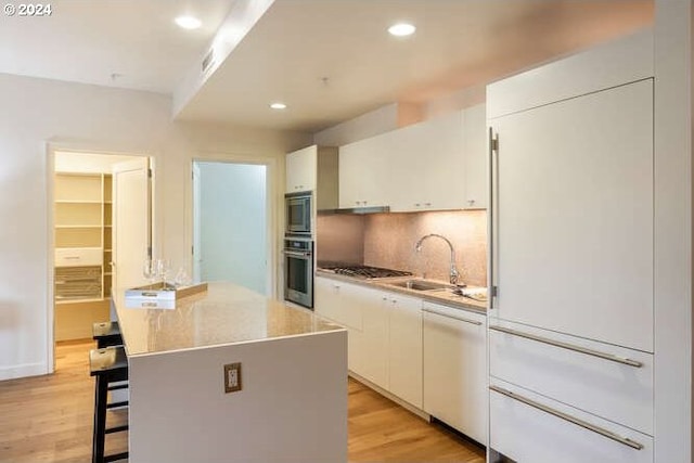 kitchen featuring stainless steel appliances, white cabinets, a sink, and light wood-style flooring