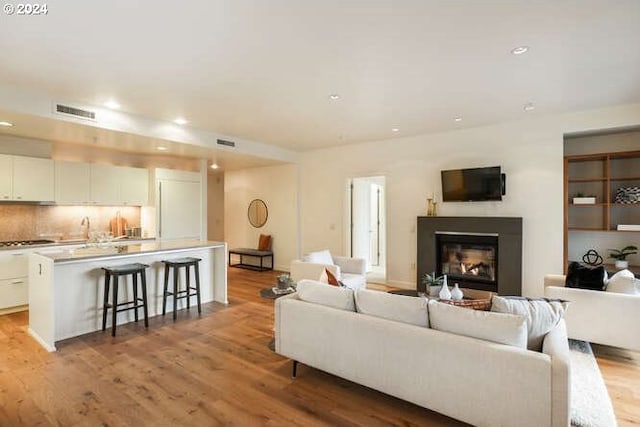 living room with light wood-type flooring, recessed lighting, visible vents, and a glass covered fireplace