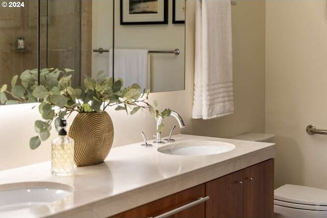 bathroom with double vanity, an enclosed shower, a sink, and toilet