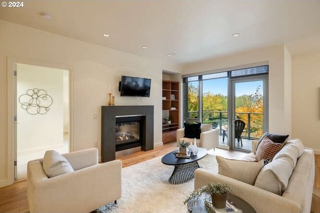 living area with wood finished floors, a glass covered fireplace, built in shelves, and recessed lighting