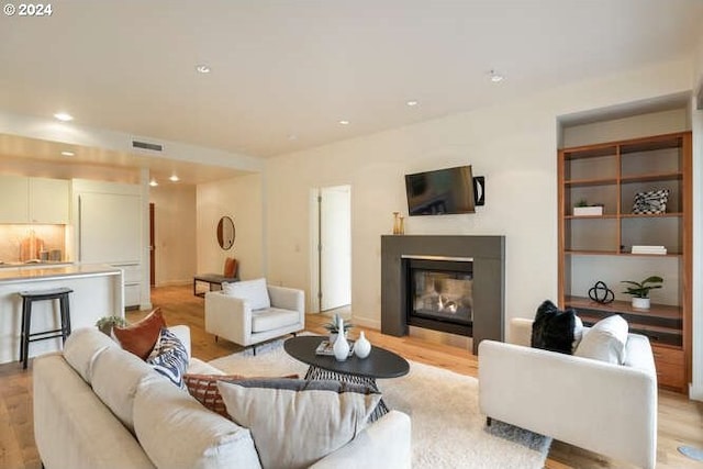 living area featuring light wood finished floors, a glass covered fireplace, visible vents, and recessed lighting