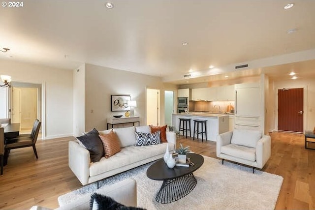 living room featuring light wood-type flooring, baseboards, a chandelier, and recessed lighting