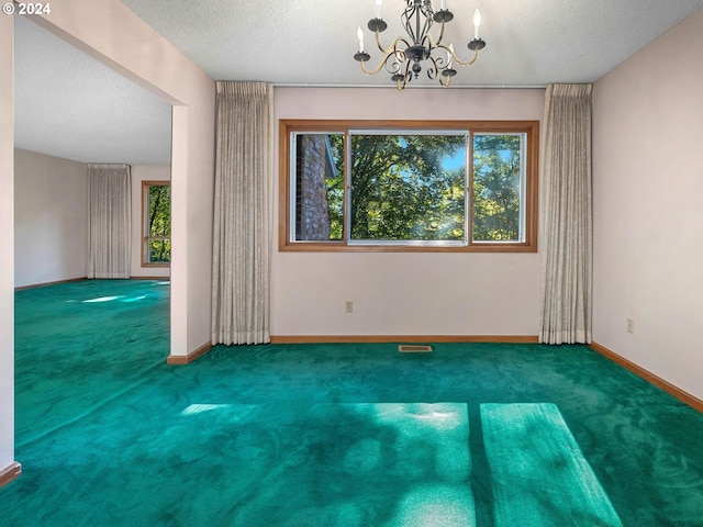 carpeted empty room featuring a chandelier and a textured ceiling