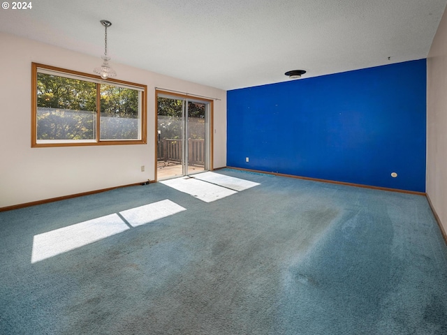 carpeted spare room with a textured ceiling and a chandelier