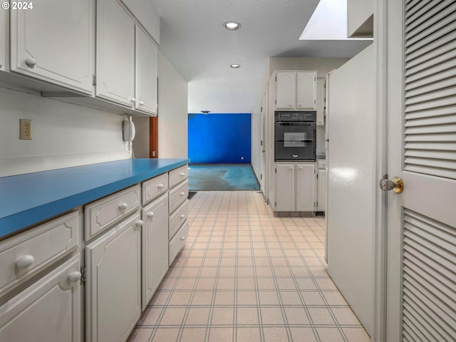 kitchen featuring a skylight, a textured ceiling, oven, and white cabinets