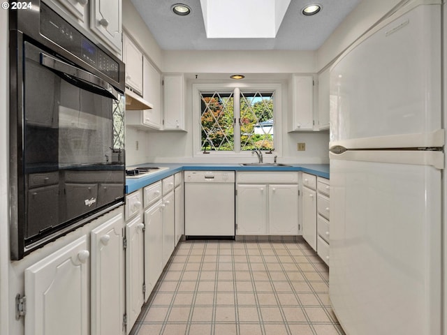 kitchen with a skylight, sink, white appliances, and white cabinetry