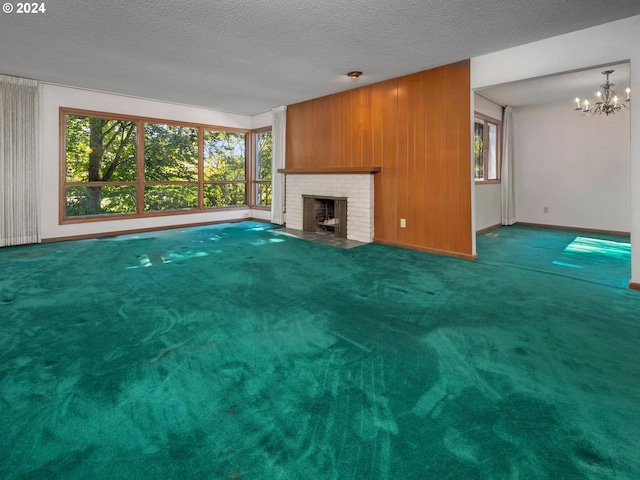 unfurnished living room with a fireplace, an inviting chandelier, wood walls, carpet, and a textured ceiling