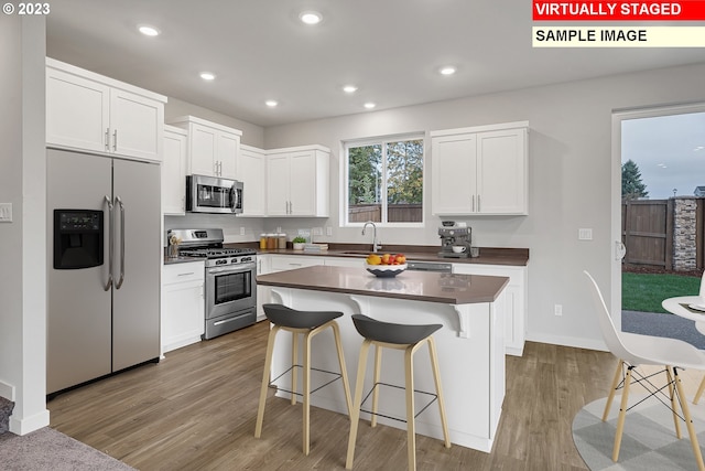 kitchen with hardwood / wood-style floors, white cabinetry, stainless steel appliances, sink, and a center island