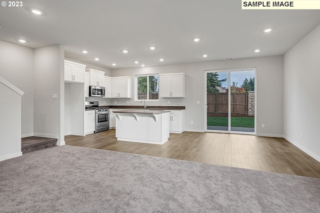 kitchen featuring a kitchen island, a kitchen breakfast bar, hardwood / wood-style floors, white cabinetry, and appliances with stainless steel finishes