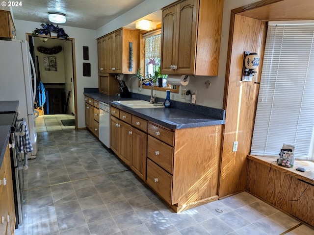 kitchen featuring brown cabinetry, white appliances, a sink, and dark countertops