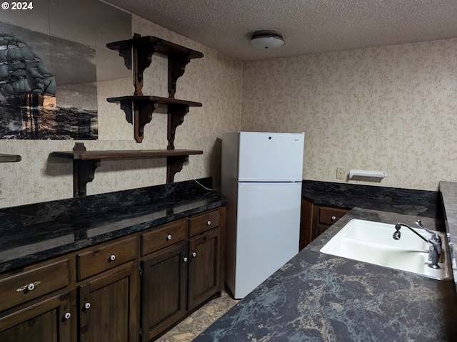 kitchen featuring sink, white fridge, dark stone counters, a textured ceiling, and dark brown cabinets