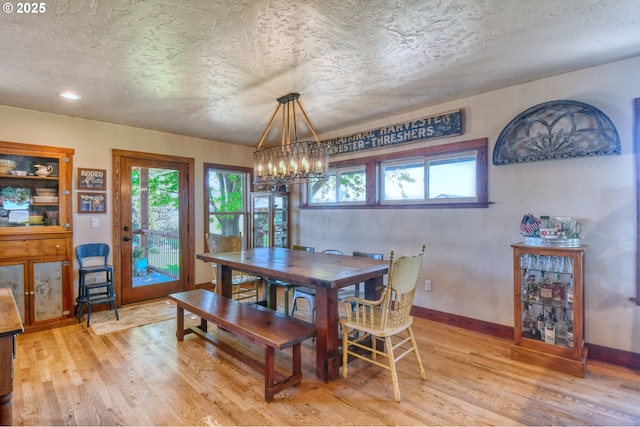 dining space with light wood-type flooring, a textured ceiling, and a notable chandelier