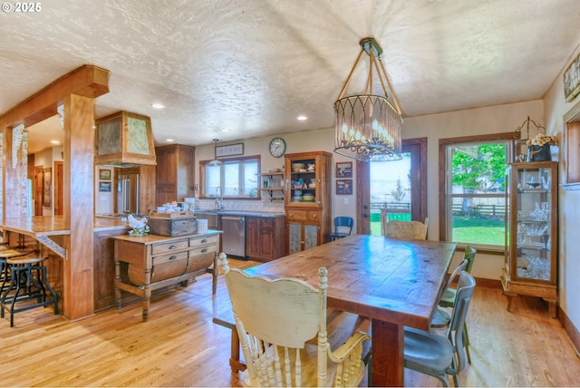 dining area with an inviting chandelier, sink, a textured ceiling, and light hardwood / wood-style flooring