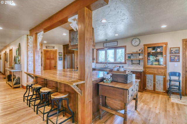 kitchen featuring light wood-type flooring, backsplash, a textured ceiling, sink, and beamed ceiling