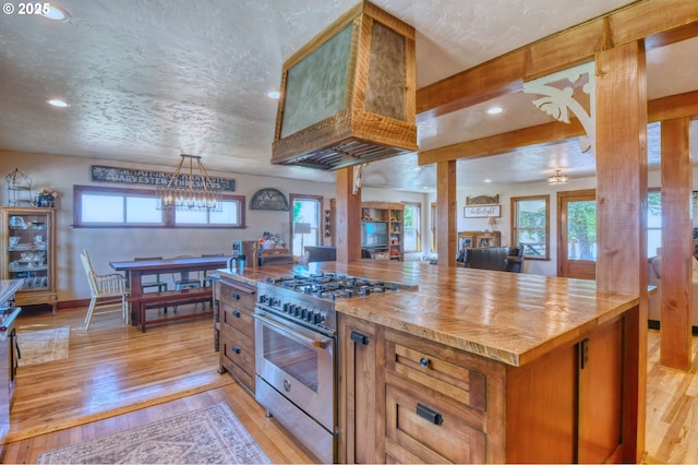 kitchen with wood counters, light wood-type flooring, premium range hood, stainless steel range, and a textured ceiling