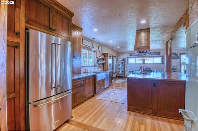 kitchen featuring light wood-type flooring, a textured ceiling, stainless steel appliances, sink, and pendant lighting