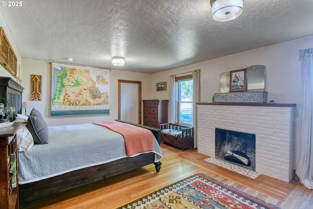 bedroom with wood-type flooring, a textured ceiling, and a brick fireplace