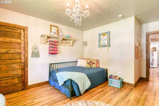 bedroom with a chandelier, a textured ceiling, and light hardwood / wood-style floors