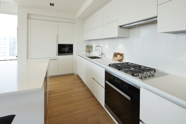 kitchen with white cabinetry, sink, oven, and range hood