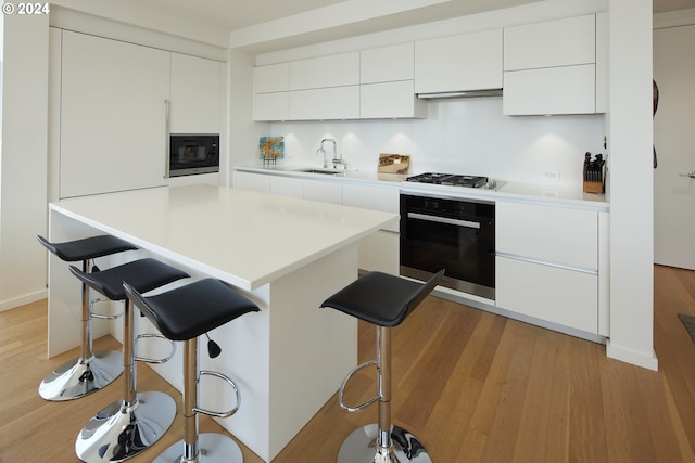 kitchen with white cabinetry, sink, a breakfast bar area, and black appliances