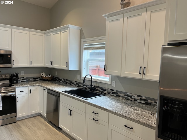 kitchen featuring stainless steel appliances, white cabinets, light stone counters, and sink