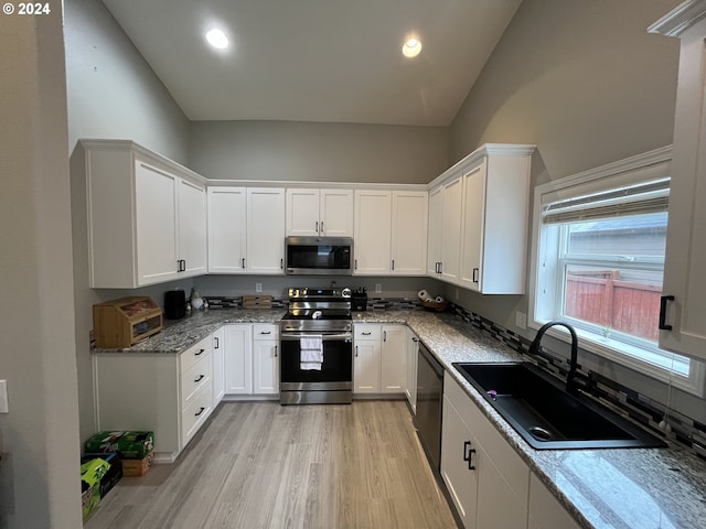 kitchen with sink, light hardwood / wood-style flooring, white cabinetry, appliances with stainless steel finishes, and vaulted ceiling