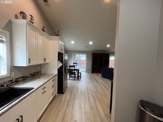 kitchen featuring white cabinets, lofted ceiling, stainless steel fridge, light hardwood / wood-style flooring, and light stone countertops