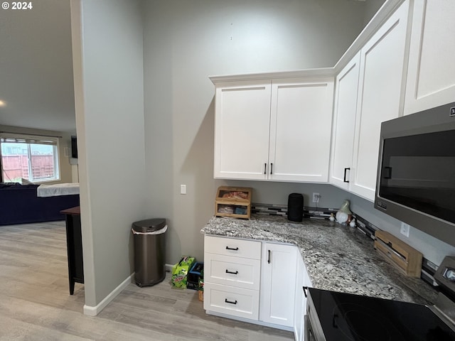 kitchen with white cabinets, stove, light hardwood / wood-style flooring, light stone countertops, and stainless steel microwave