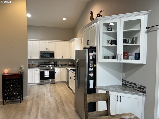 kitchen with appliances with stainless steel finishes, white cabinetry, light stone countertops, lofted ceiling, and light hardwood / wood-style flooring