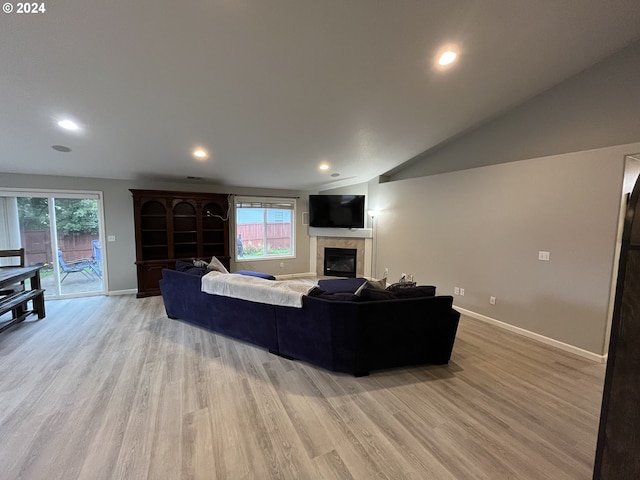 living room with light wood-type flooring, lofted ceiling, and a tiled fireplace