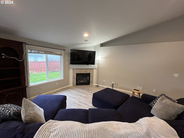 living room with light wood-type flooring, a tile fireplace, and lofted ceiling