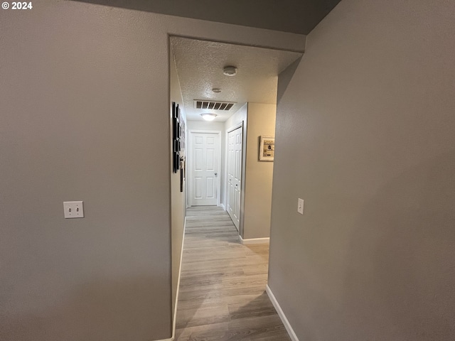 corridor with light hardwood / wood-style flooring and a textured ceiling