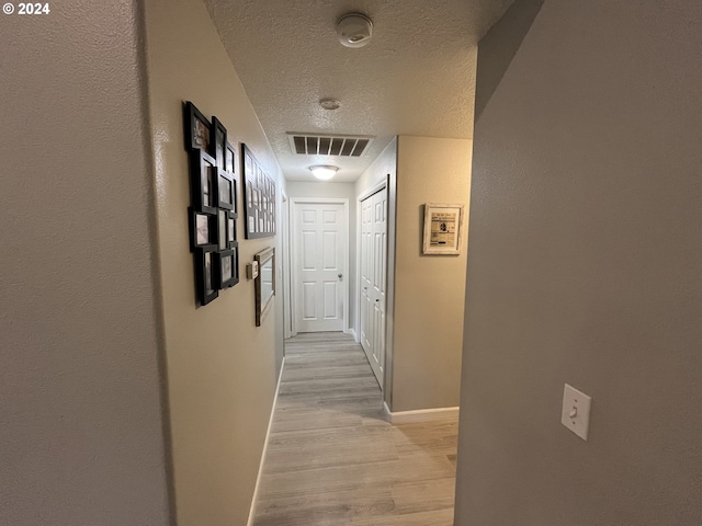 hallway with light hardwood / wood-style floors and a textured ceiling