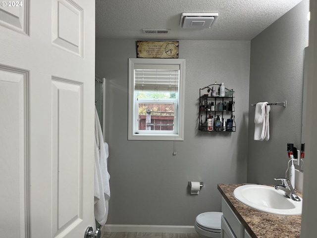 bathroom with a textured ceiling, vanity, and toilet